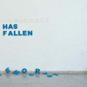 Wand mit aufgehängten Buchstaben die die Wörter "Has Fallen" bilden. Auf dem Boden liegen die Buchstaben für das Wort "Democracy"