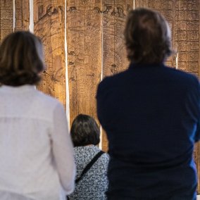 Eine Frau mit weissem Hemd und ein Mann mit blauem Hemd stehen vor den Tikal Tafeln der Maya aus Guatemala in der Ausstellung "Memory"